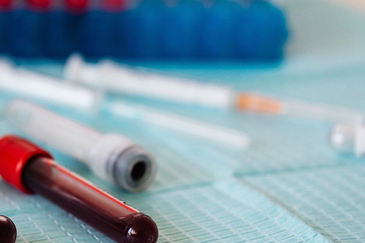 Blood sample tubes with red and lavender caps, syringes and a tube rack on a blue paper sheet