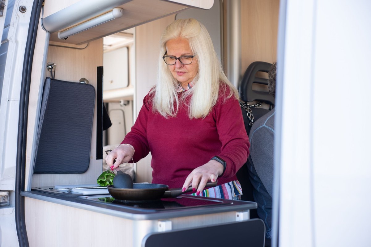 Woman in a red sweater cooking a green pepper in a frying pan in a camper van kitchen