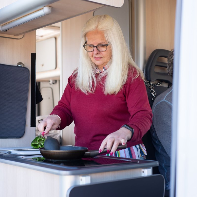 Woman in a red sweater cooking a green pepper in a frying pan in a camper van kitchen