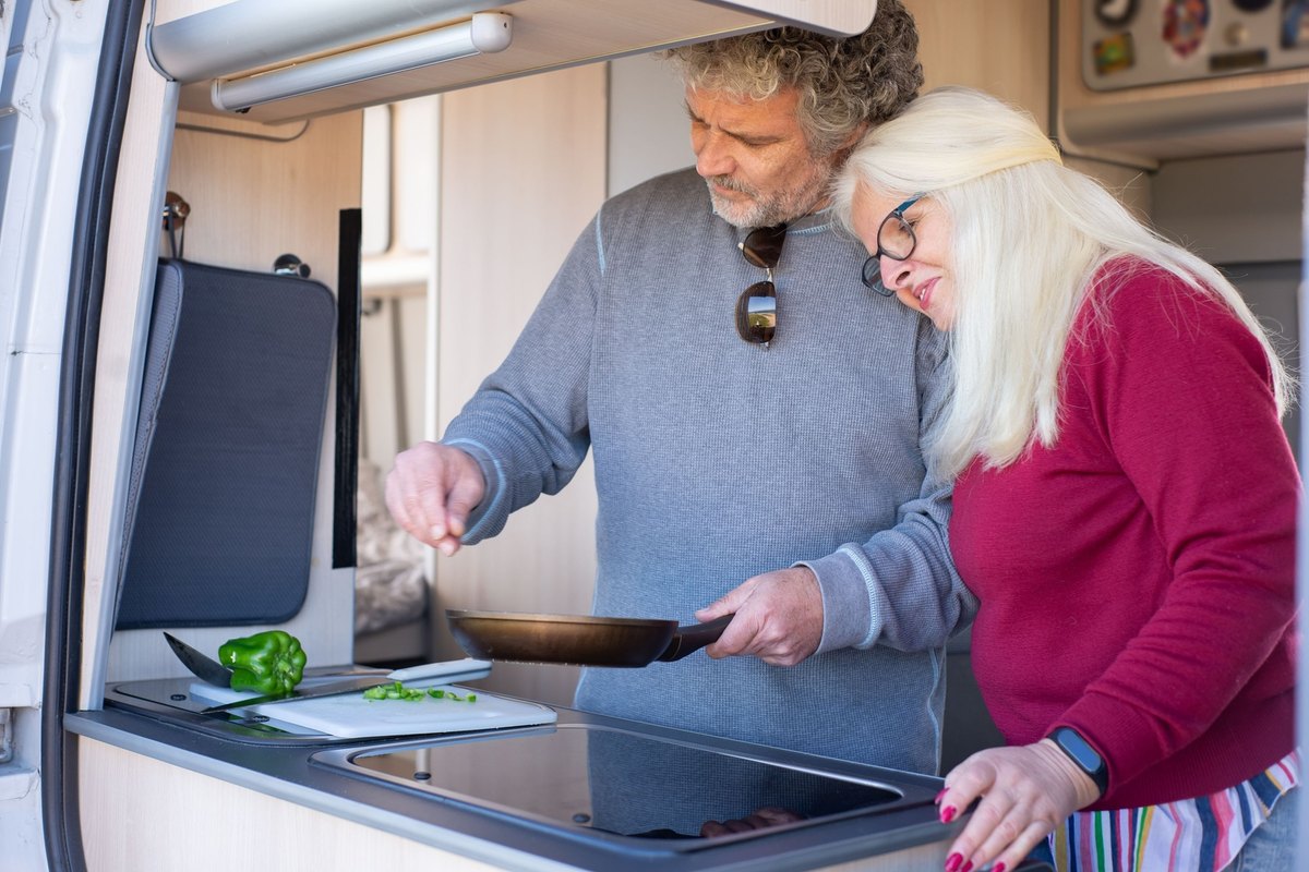 Man and woman cooking together in a van kitchen as she leans on his shoulder