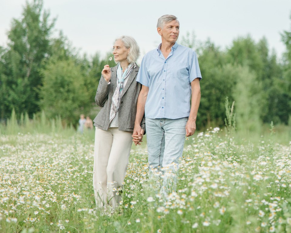 Older couple holding hands in a meadow of white daisies