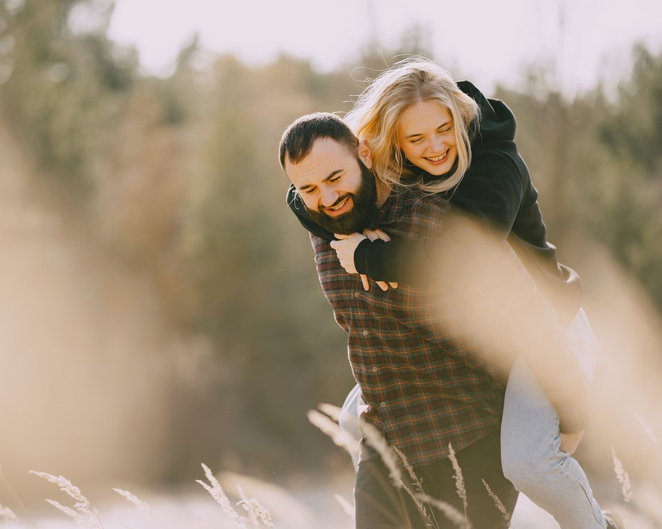 Laughing man carrying a laughing woman on his back through a sunlit field