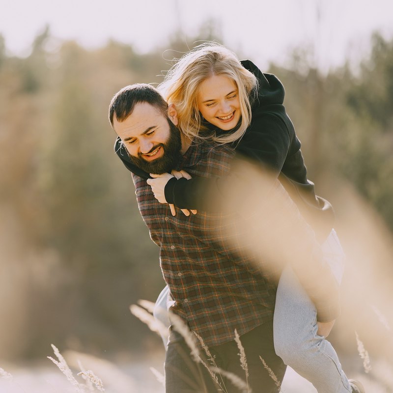 Laughing man carrying a laughing woman on his back through a sunlit field