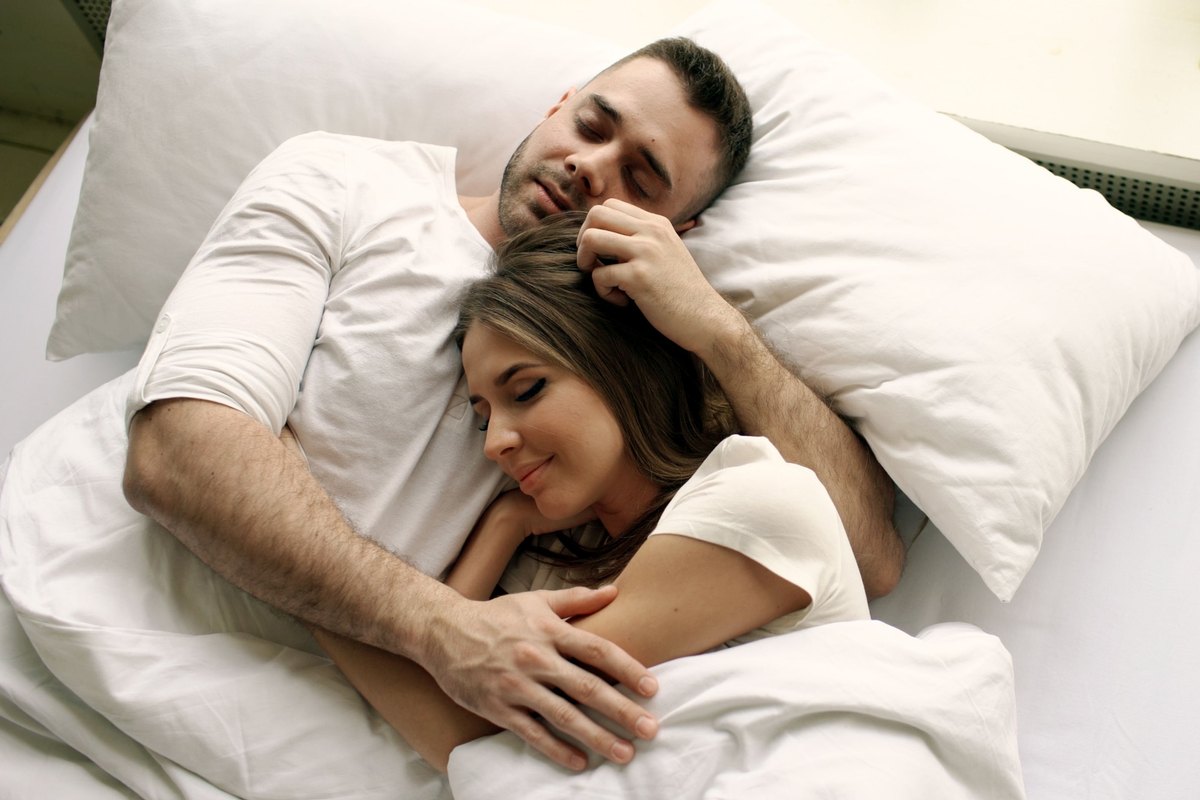 Man and woman asleep and cuddling in a bed with white sheets