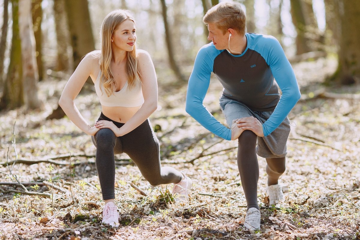 Woman and man in lunge stretches looking at each other on a forest floor