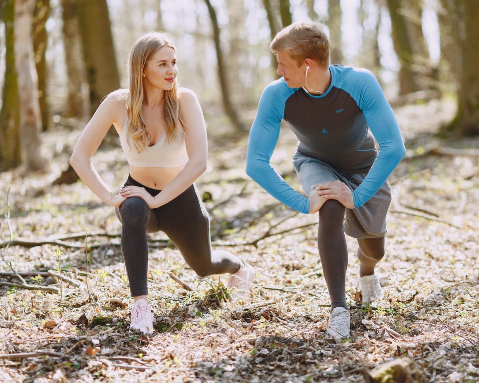 Woman and man in lunge stretches looking at each other on a forest floor