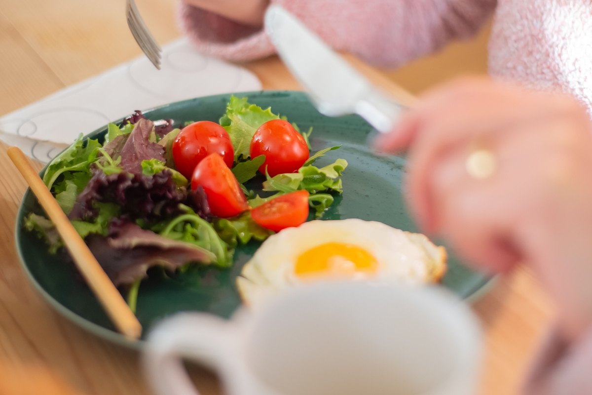 Fried egg with salad and halved tomatoes on a green plate while a person eats