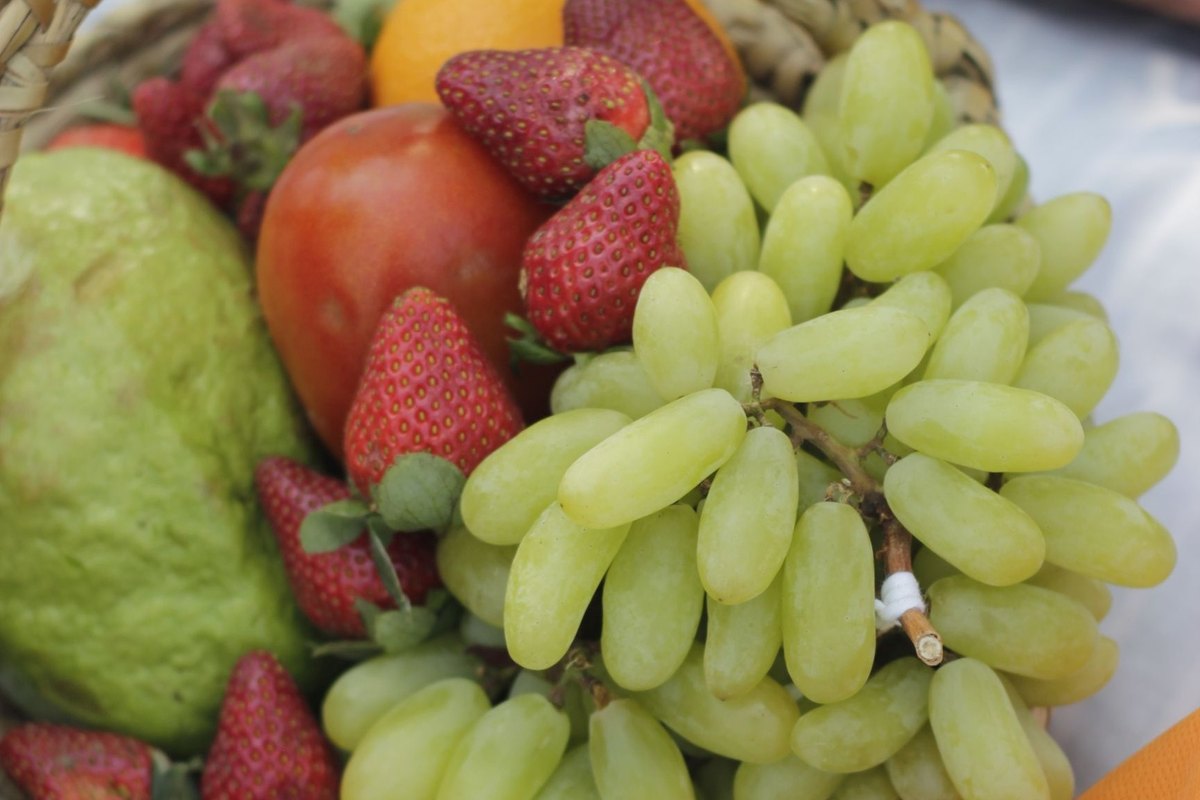 Woven basket of fresh strawberries, green grapes and other fruit