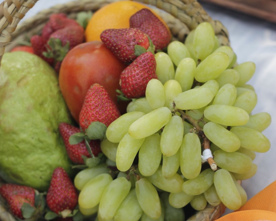 Woven basket of fresh strawberries, green grapes and other fruit