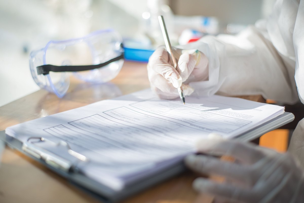Gloved hand writing on a form on a clipboard beside safety goggles