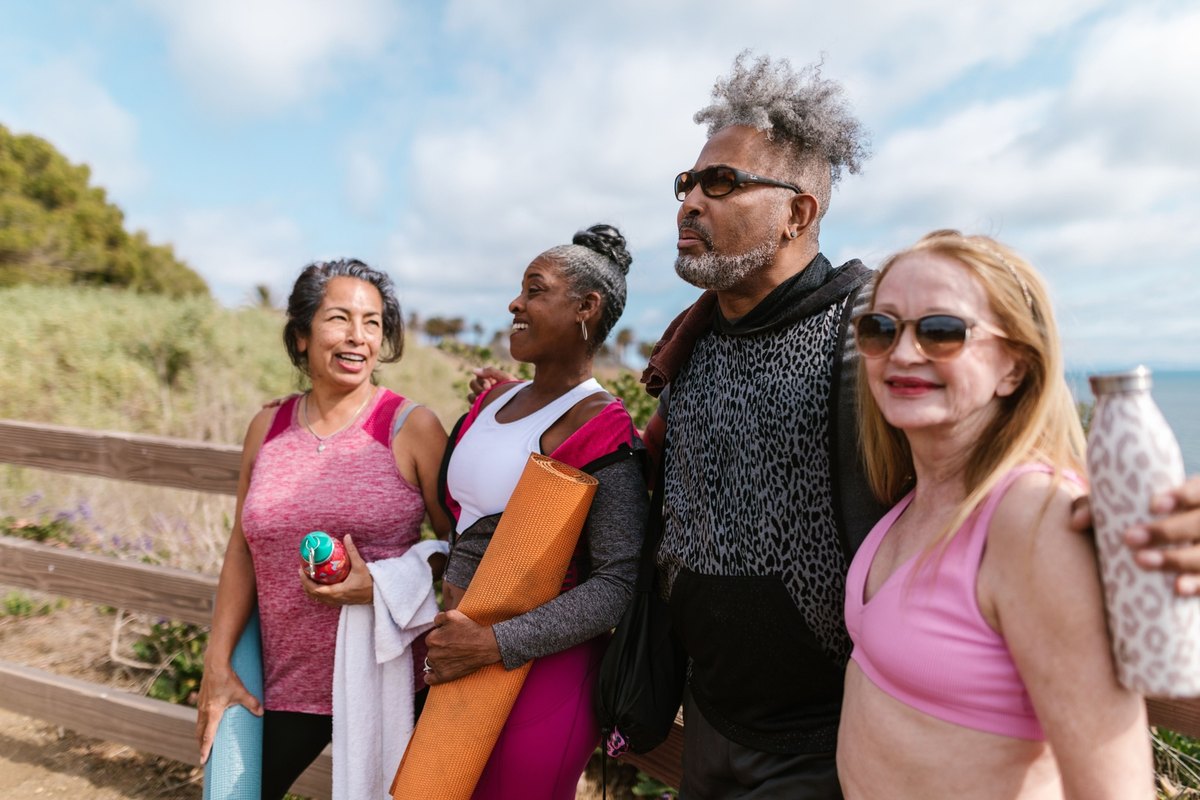 Four older adults with yoga mats and water bottles laughing together on a coastal path