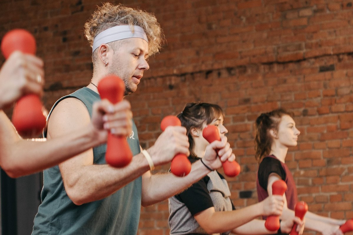 Three people lunging while holding red dumbbells in an exercise class against a brick wall