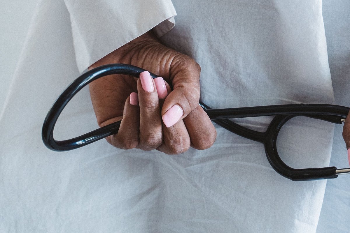 Hand in a white coat holding the looped tubing of a black stethoscope