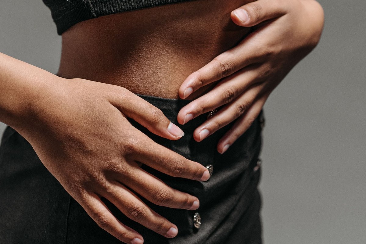 Woman in black clothing with both hands resting on her stomach