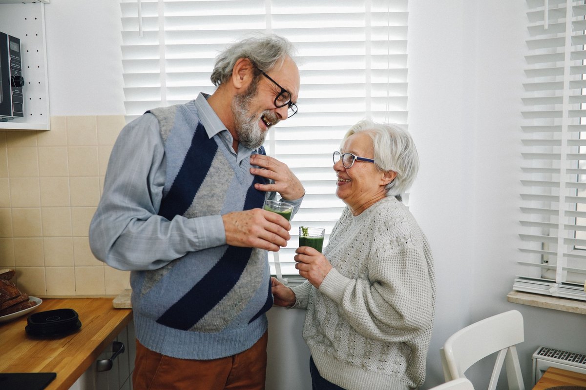 Man and woman laughing together while holding glasses of green smoothie
