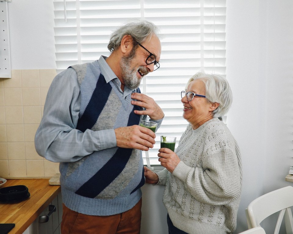 Man and woman laughing together while holding glasses of green smoothie