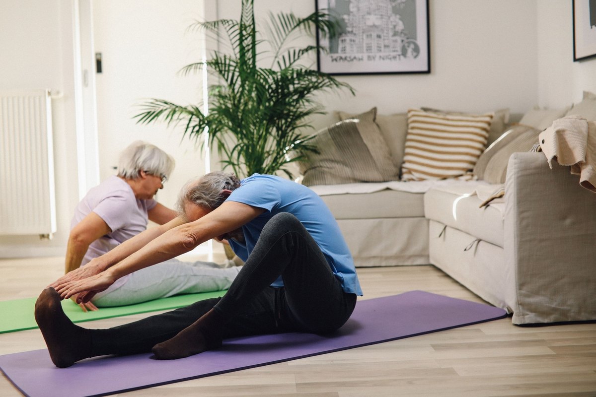 Man and woman stretching their legs on yoga mats in a living room