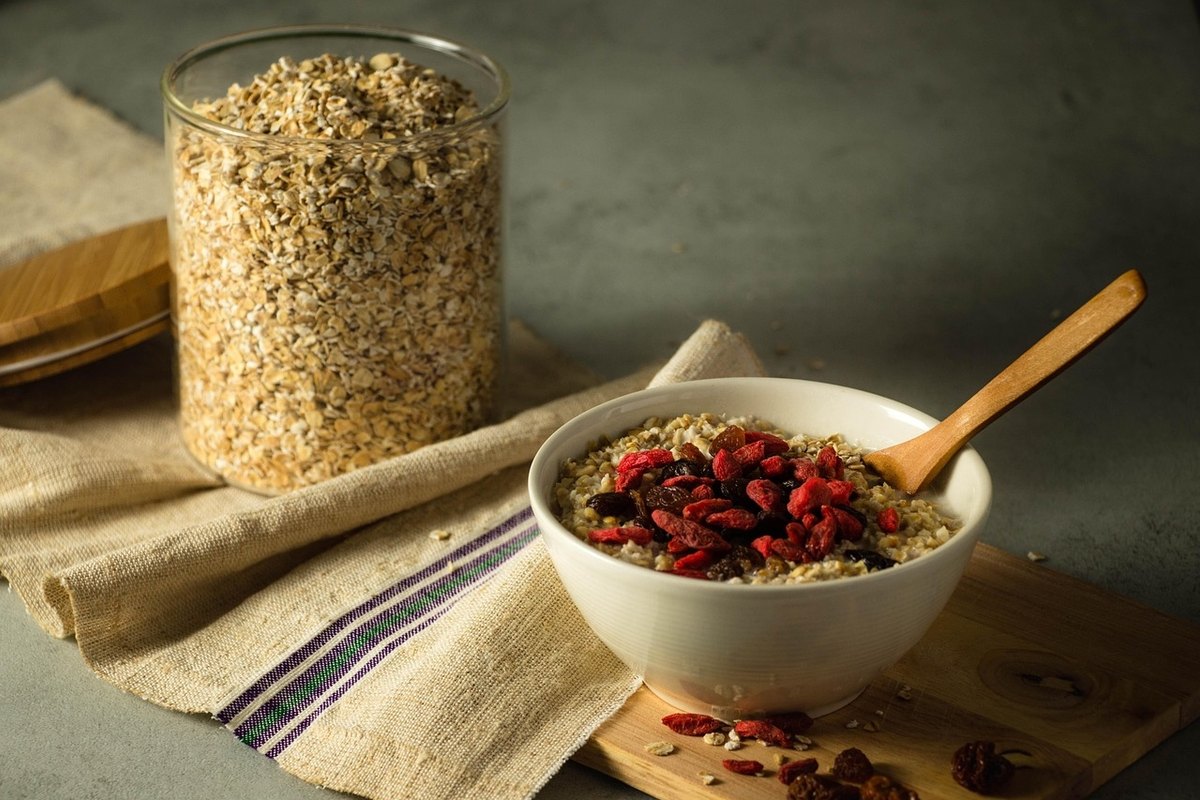 White bowl of cooked oats topped with red goji berries beside a glass jar of rolled oats