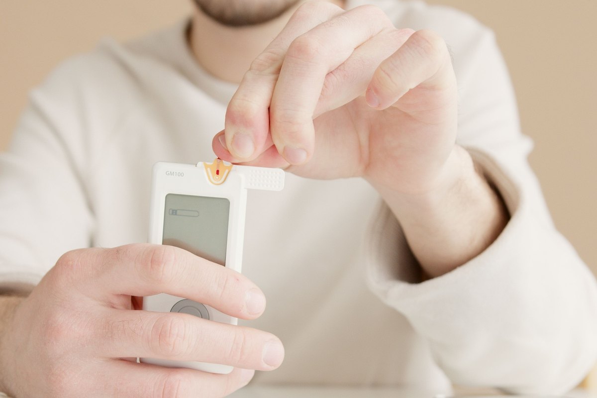 Person holding a white blood glucose meter and touching a test strip to it