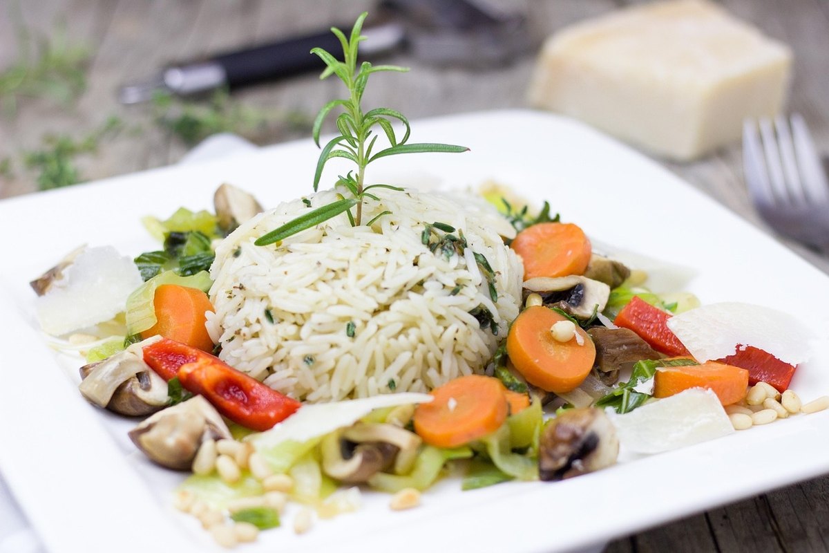 Square white plate of rice with sliced carrots, mushrooms and red pepper