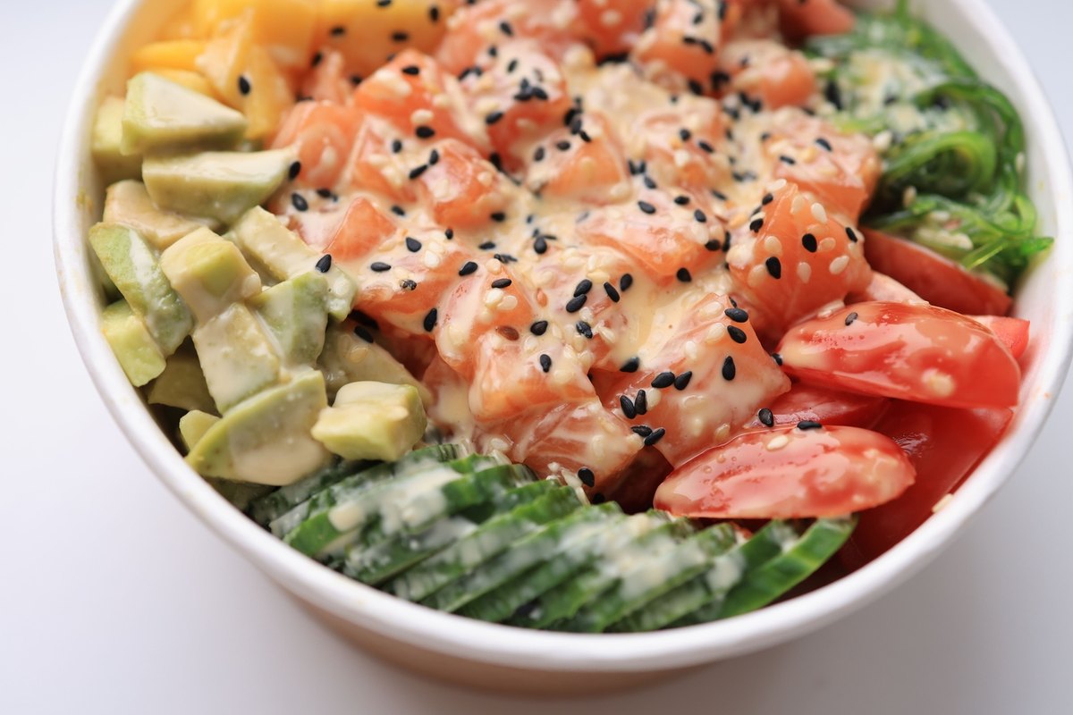 White bowl of diced salmon with avocado, mango, seaweed salad, tomato and cucumber