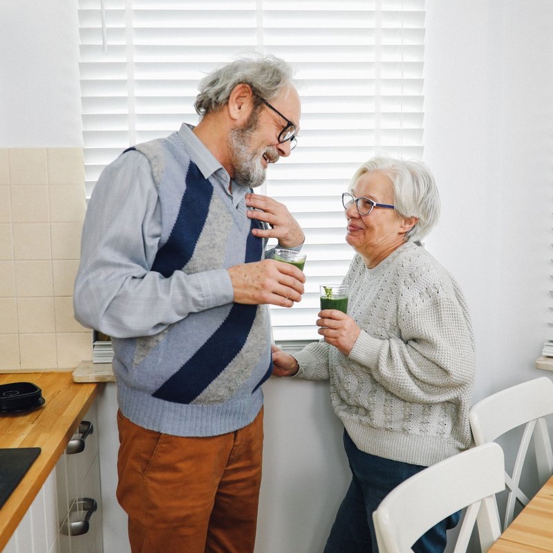 Man and woman smiling at each other while holding glasses of green smoothie