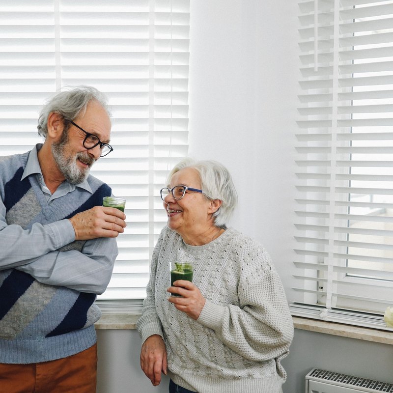 Man and woman holding glasses of green smoothie and smiling at each other