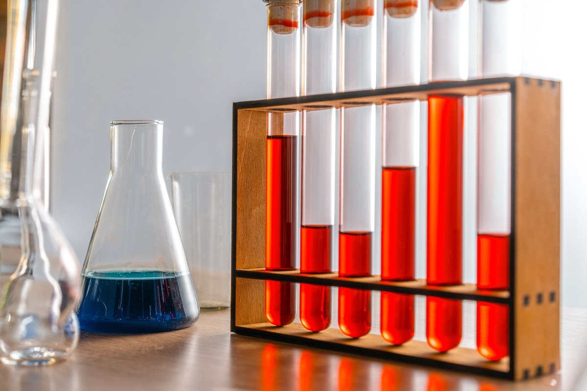 Rack of glass test tubes with red liquid beside a flask of blue liquid on a laboratory bench