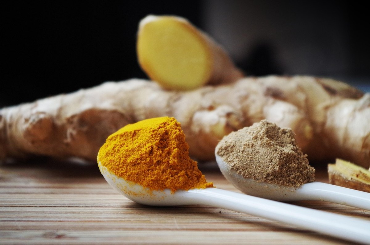 Spoons of turmeric and ground ginger in front of a whole ginger root
