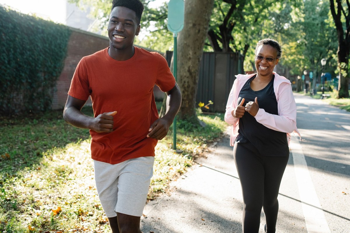 Young man and older woman jogging side by side on a park path, both smiling