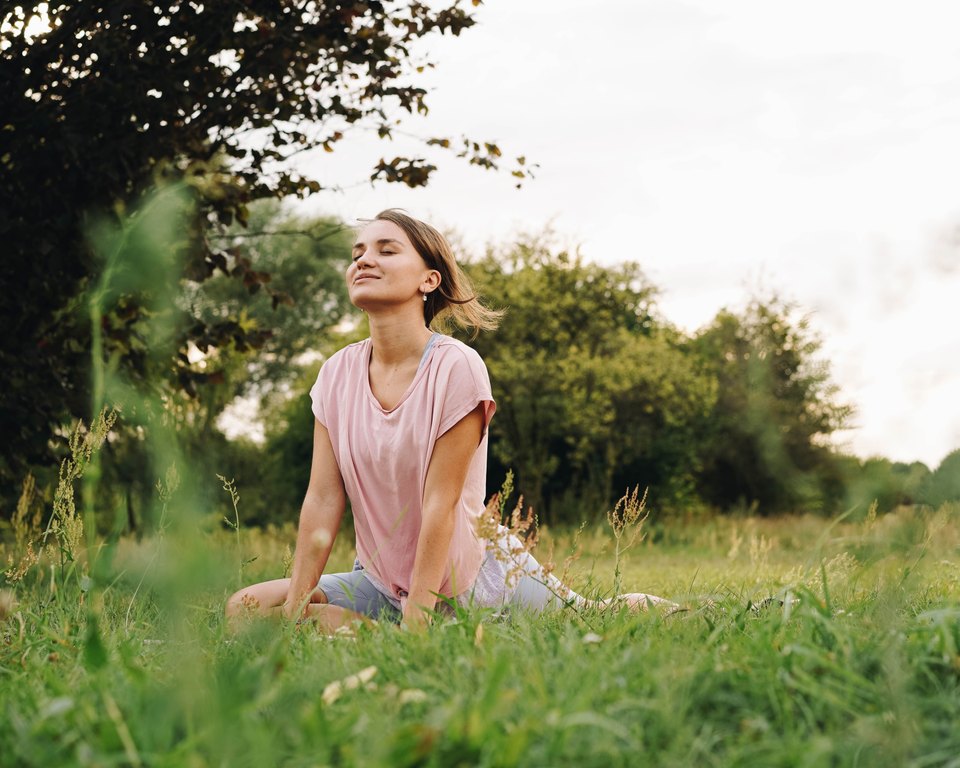 Woman with her eyes closed and chin lifted, stretching in a yoga pose on the grass in a meadow