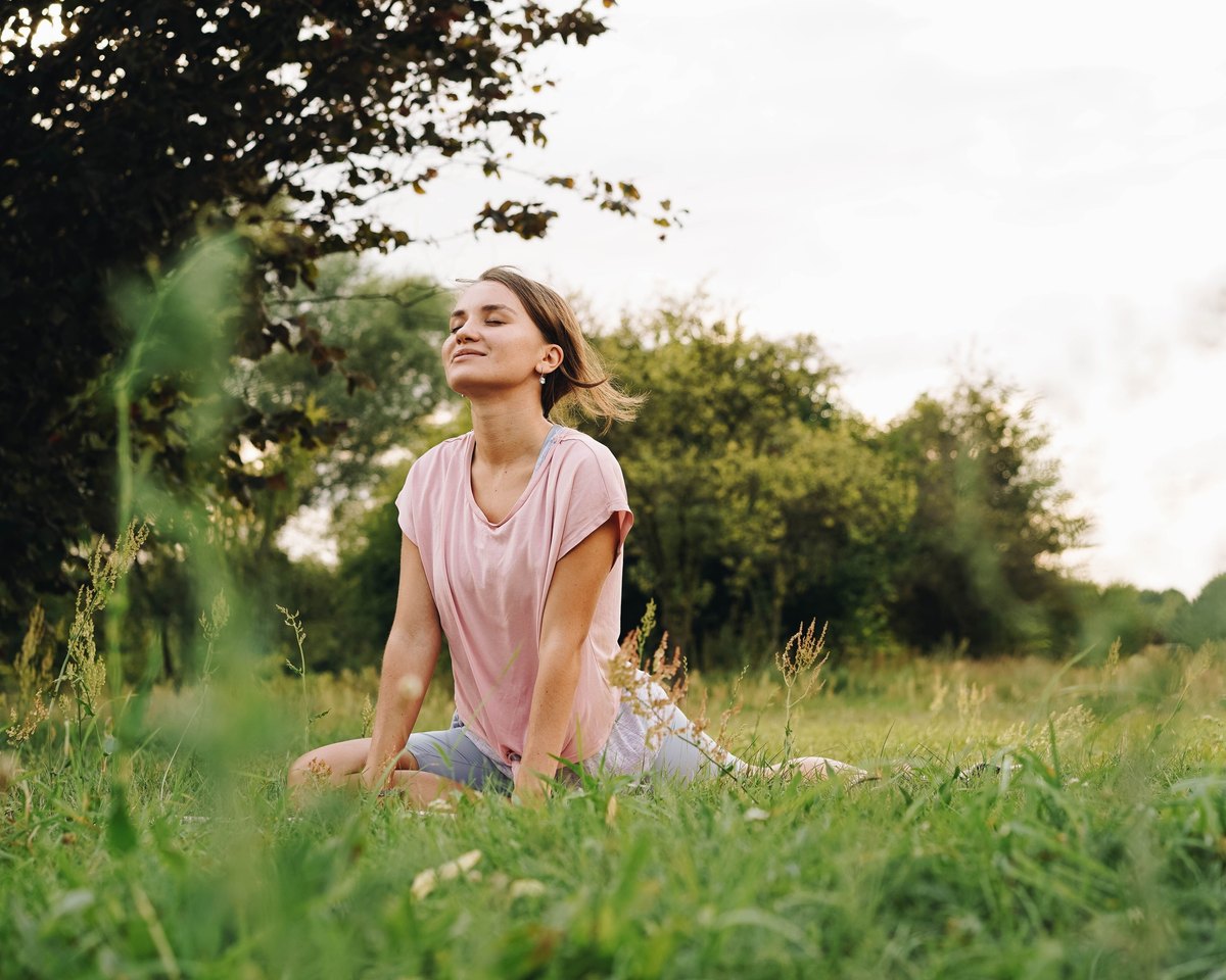 Woman with her eyes closed and chin lifted, stretching in a yoga pose on the grass in a meadow