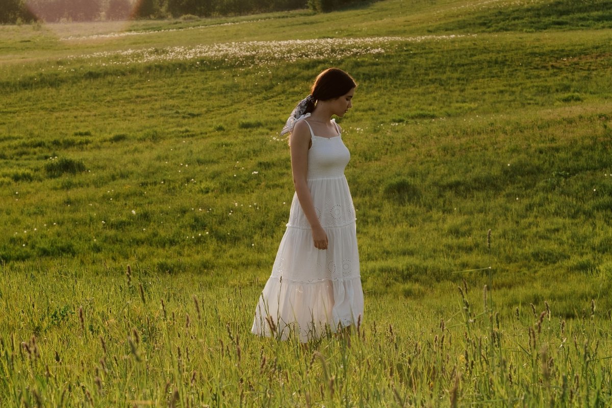 Woman in a white sundress walking through tall grass in a green meadow