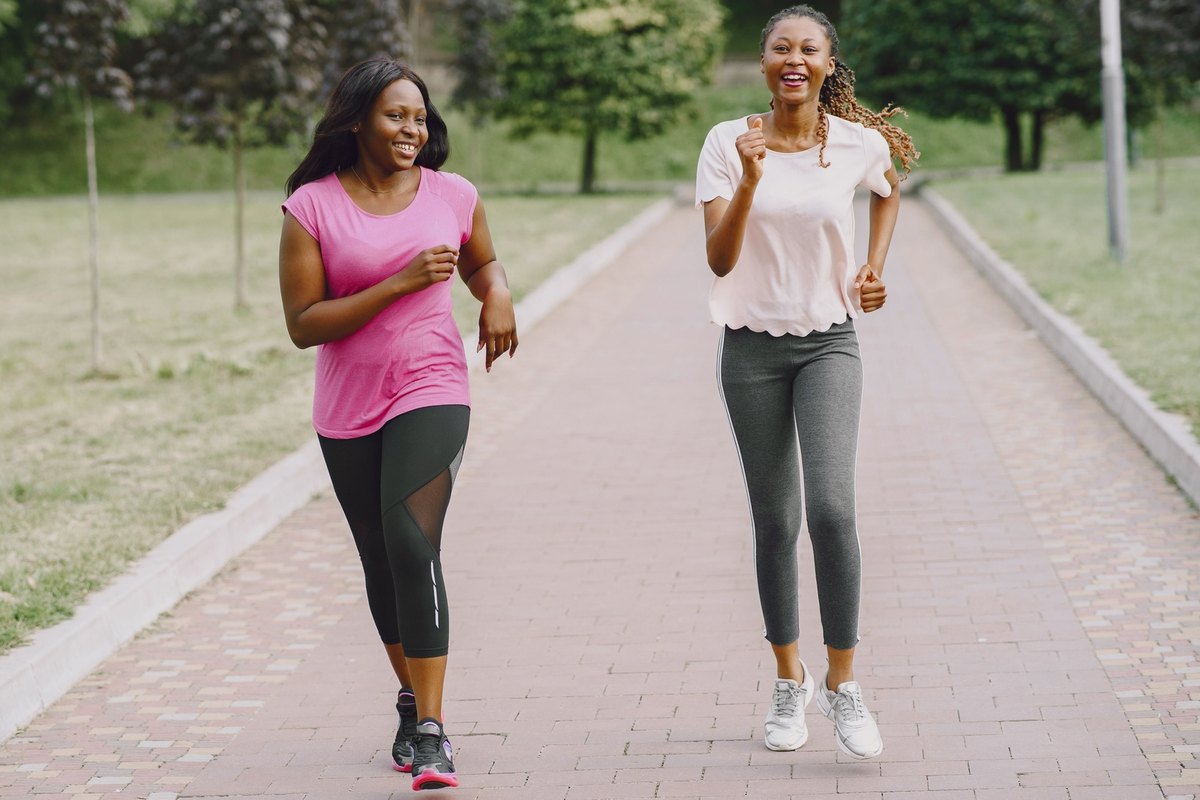 Two smiling women jogging side by side on a brick path in a park