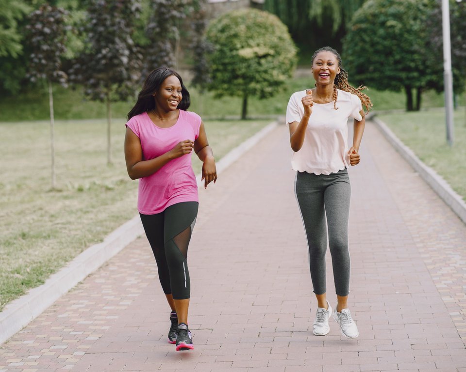 Two smiling women jogging side by side on a brick path in a park