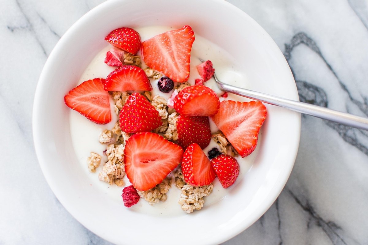 White bowl of yogurt topped with granola and halved strawberries